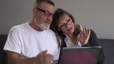 Mutlu orta yaşlı karı koca evde dizüstü bilgisayar kullanıyor, gülümseyen gri saçlı adam ve kadın bilgisayar ekranına bakıyor, video görüşmesi yapıyor, internette sohbet ediyorlar.