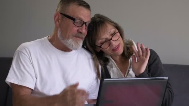 Feliz de mediana edad esposa y marido utilizando el ordenador portátil juntos en casa, sonriendo gris hombre y mujer mirando a la pantalla de la computadora, haciendo videollamada, charlando en línea — Vídeos de Stock
