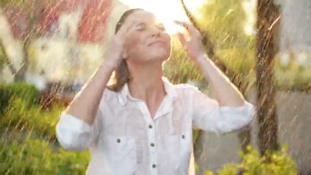 美丽的女人与湿头发享受雨和仰望天空。漂亮的女人在夏日花园有很多乐趣。雨天快乐暖色的彩色视频。叶子与雨滴. — 图库视频影像