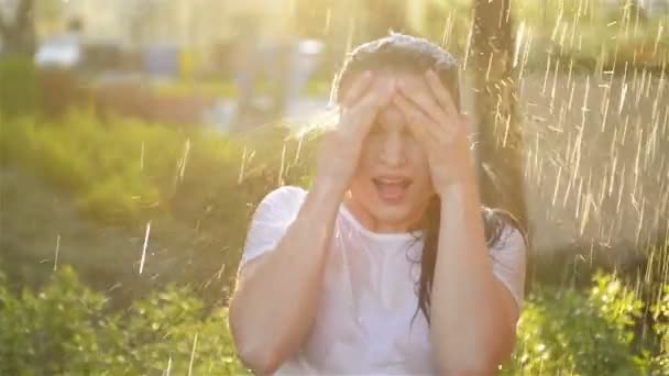 Jovem mulher sorridente está sob chuva fresca no verão. Ela se diverte muito passando suas férias na natureza . — Vídeo de Stock