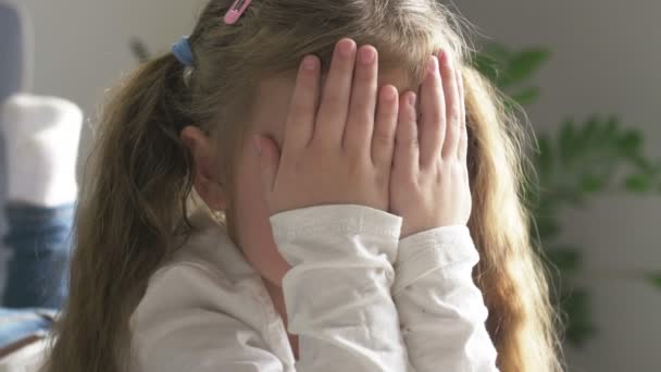 Söt liten flicka täcker sitt ansikte med händer hemma. Leker kurragömma, tjuvkikar. Närbild — Stockvideo