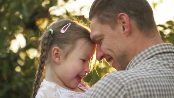 Egy portré apáról, ahogy a kezében tartja a kislányt, és megöleli egymást a szabadban. Apa ölelkezik és csókolózik a lányával. Apák napja — Stock videók
