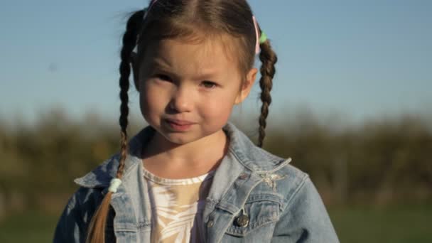 Κοντινό πορτραίτο νεαρό κοριτσάκι που δείχνει σοβαρό στοχαστικό, παιδί στο ηλιόλουστο πάρκο — Αρχείο Βίντεο