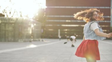 Mutlu kadın müzik dinliyor ve dışarıda kulaklıkla dans ediyor. Kentsel arka planda kıvırcık saç modeli ile rahat giysiler içinde Kız.