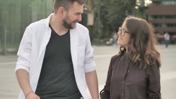 Glad att vara tillsammans. Bakifrån av vackra unga par hålla händer och titta på varandra med leende medan du går genom stadsgatan — Stockvideo