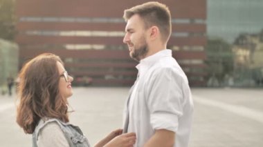 Genç bir adam sokakta yürüyen çekici bir kızla tanışıyor ve ona sarılıyor. Günbatımı şehir arka planı, yakın çekim. Yavaş çekim