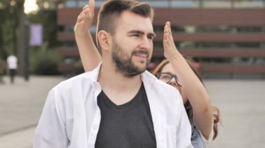 Genç bir kız bir adamın gözlerini kapatır ve güler. İlişki, dostluk ve aşk teması.