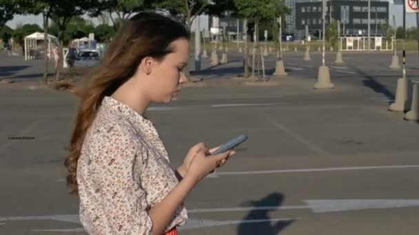 Hermosa chica caucásica caminando por la calle captura su atención por el teléfono inteligente y chocó con un poste de luz. Concepto - adicción a teléfonos inteligentes . — Vídeo de stock