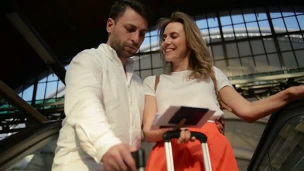 Unga glada par reser sig med bagage på rulltrappan till avreseområdet på flygplatsen under sin sommarsemester. — Stockvideo