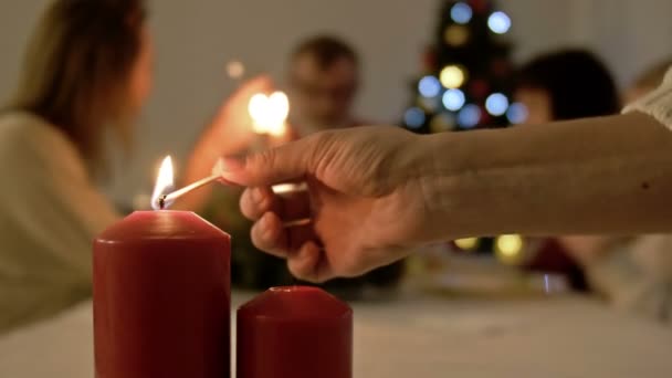 女性はクリスマスや新年の夕食のために提供されるテーブルの上にろうそくを点灯。背景にあるテーブルと大きな家族 — ストック動画