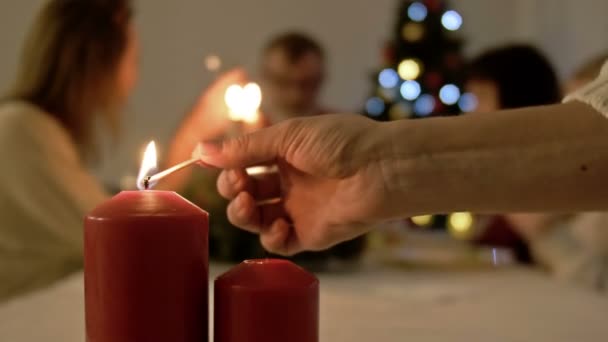 Vrouw die kaarsen aansteekt op tafel geserveerd met Kerstmis of Nieuwjaar diner. Tafel geserveerd en grote familie op de achtergrond — Stockvideo