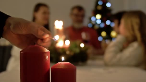 Comida familiar de Navidad. Un joven enciende las velas en la mesa de Navidad. Familia grande y árbol de Navidad en el fondo — Vídeos de Stock