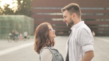 Genç bir adam sokakta yürüyen çekici bir kızla tanışıyor ve ona sarılıyor. Günbatımı şehir arka planı, yakın çekim. Yavaş çekim