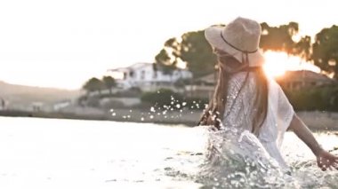 O okyanusta duruyor ve yan yana döner gibi elbise kız elleriyle turkuaz su sıçrayan. Yaz tatilinin tadını çıkaran kadın turist.