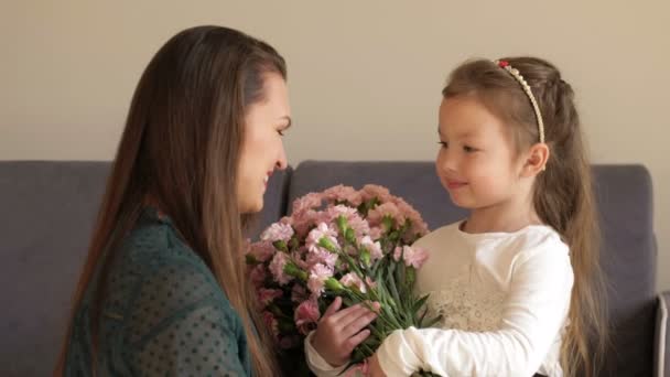 Lycklig flicka som ger blommor och kramar sin mamma hemma. Mödrars dag koncept — Stockvideo