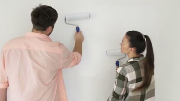 Junge Familie macht Reparaturen im neuen Haus. schönes Paar - Wandmalerei in der Wohnung. Mann und Frau machen Dekoration Zimmer, küssen und Spaß haben. — Stockvideo