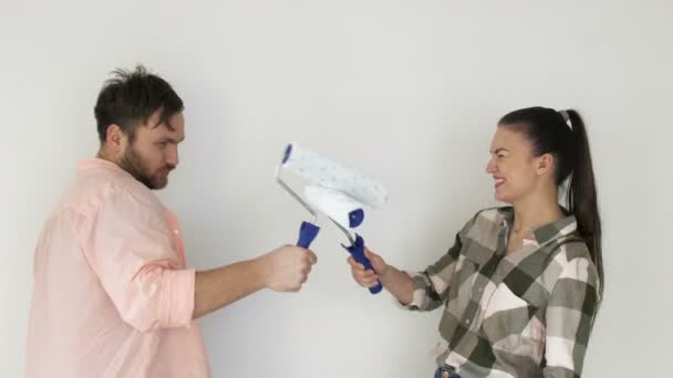 Hermosa pareja pintar las paredes en un nuevo apartamento, riendo y divirtiéndose. Joven familia hace reparaciones en su nuevo piso — Vídeo de stock