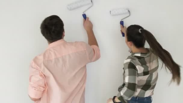 Parede de pintura familiar jovem positivo em casa nova, rindo e dançando juntos — Vídeo de Stock