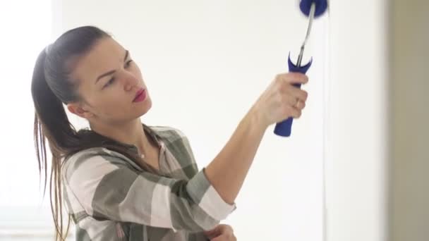 Portret van een jonge mooie vrouw die thuis een muur schildert. Werk met een Roller. Appartement Renovaties. — Stockvideo