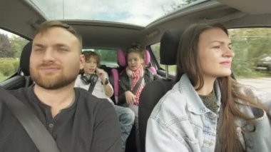 Front view of happy loving parents and their excited kids smiling driving a car in the city. Young family traveling abroad by auto.