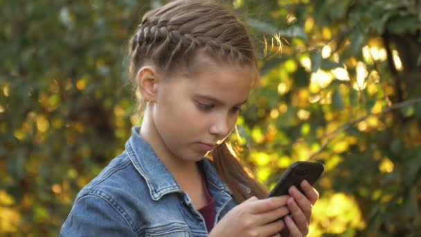 Teen girl alone using a mobile phone against the background of a apple garden. Smartphone addiction — Stock Video