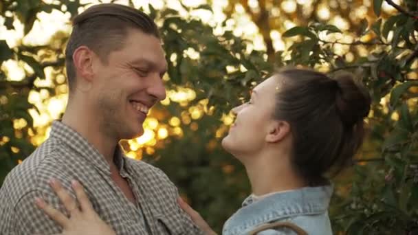 Szczęśliwy mężczyzna i dziewczyna całują się i przytulają o zachodzie słońca w parku. Kochający mężczyzna i kobieta w romantycznym otoczeniu w ogrodzie jabłkowym. Pojęcie relacji rodzinnych. Zwolniony ruch. — Wideo stockowe