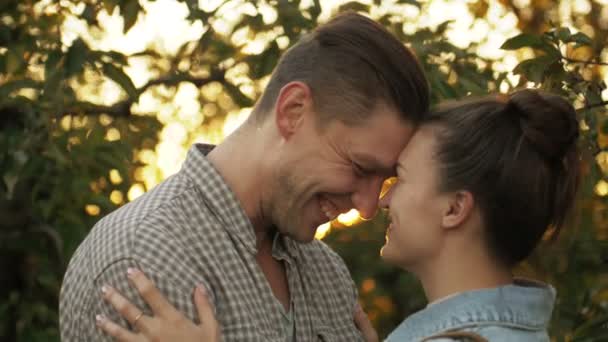 Uomo e ragazza felici si baciano e si coccolano al tramonto nel parco. Amare l'uomo e la donna in un ambiente romantico nel giardino delle mele. Concetto di relazioni familiari. Rallentatore . — Video Stock