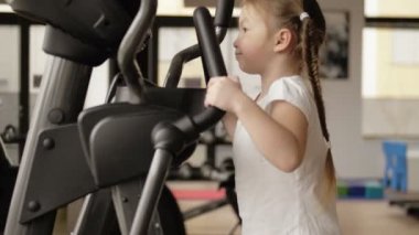 Çocuk bir spor salonunda simülatörlerle meşgul. Vücut geliştirme konsepti, spor giyim.