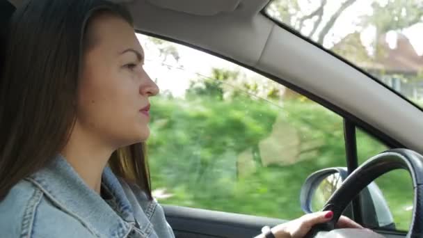 Porträt einer schönen jungen Frau, die mit dem Auto durch die sonnige Großstadt fährt. Kamerafahrt vom Beifahrer aus. — Stockvideo