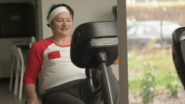 Mujer de mediana edad haciendo ejercicios de cardio en bicicleta de papelería en un gimnasio o gimnasio . — Vídeos de Stock