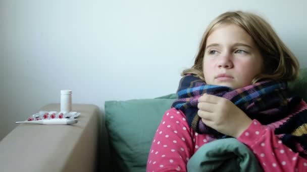 Домашнє лікування. Дівчинка з шарфом хворіє вдома, нежить і грип. Тепло одягнений і покритий ковдрою. Дме їй ніс у серветку. Інфекція, епідемія — стокове відео