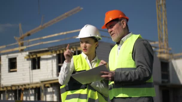 Mann und junge Frau mit Helmen vor dem Hintergrund eines im Bau befindlichen Hauses. — Stockvideo