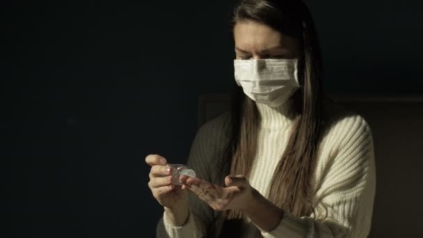 Young woman in a medical mask sprayes an antiseptic on the hands. Precautionary measures. On a black background. — Stock Video