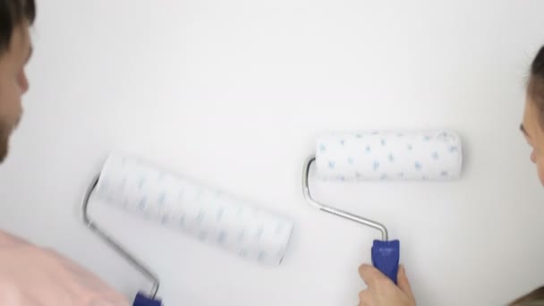 Uomo e donna dipingono pareti con rulli. Coppia allegra su uno sfondo di una parete bianca . — Video Stock