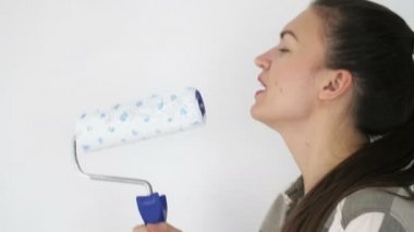 Genç kadın şarkı söylüyor. Mikrofon olarak boya silindiri kullanıyor..