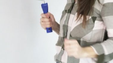 Genç kadın dans ediyor ve şarkı söylüyor. Mikrofon olarak boya silindiri kullanıyor..