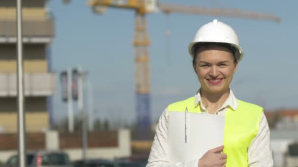 Vrouwenbouwer in beschermende kleding op de bouwplaats. Jonge vrouw heeft een map met documenten en glimlachen. — Stockvideo