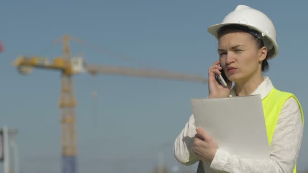 Budowlaniec w kasku trzyma teczkę z dokumentami i rozmawia przez telefon. Sukces kobiety biznesu. — Wideo stockowe