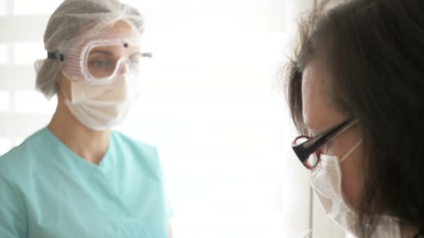 Enfermeira em uma máscara médica, óculos e luvas mede a temperatura do paciente com um termômetro infravermelho sem contato . — Vídeo de Stock
