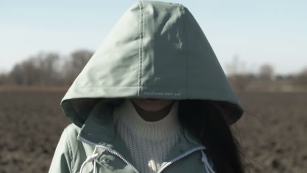 Close up portrait of hooded young woman looking at camera, field background — Stock Video