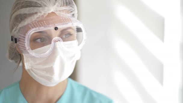 Porträtt av en sjukvårdare i medicinsk mask, skyddsglasögon och engångshatt. — Stockvideo
