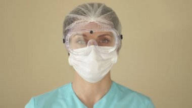Kadın doktor ya da hemşire tıbbi maske ve güvenlik gözlüklerini çıkarır. Yorgun görünüyorsun..