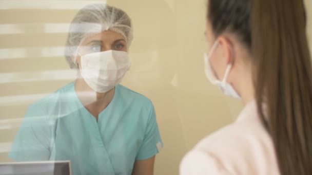 Na sala de espera do hospital, a enfermeira de plantão está conversando com o paciente. Enfermeira e paciente em máscaras médicas. Protecção contra a infecção viral . — Vídeo de Stock