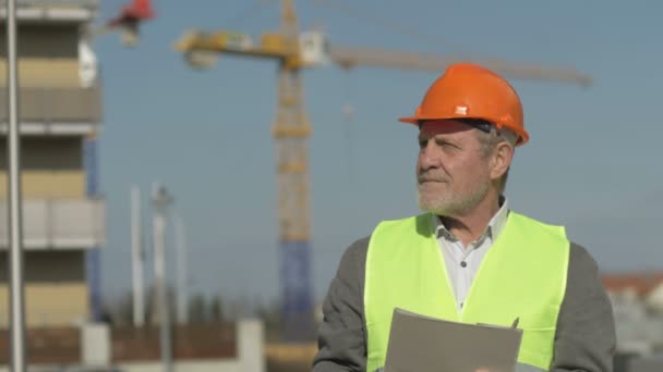 Äldre förman i uniform mot bakgrund av en byggnad under uppförande. — Stockvideo