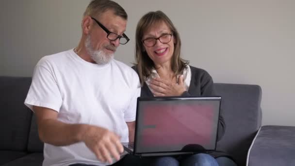 Feliz pareja de mediana edad riendo hablando abrazando el uso de la computadora portátil juntos mirando la pantalla de la computadora, haciendo una llamada en línea en casa — Vídeos de Stock