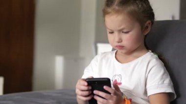 Evdeki koltukta oturan sıradan bir çocuk, oynuyor ve cep telefonuna dokunuyor.