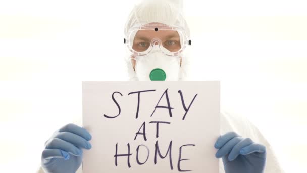 Mężczyzna w kombinezonie ochronnym trzyma znak "Zostań w domu". Epidemia, pandemia koronawirusa covid 19. — Wideo stockowe