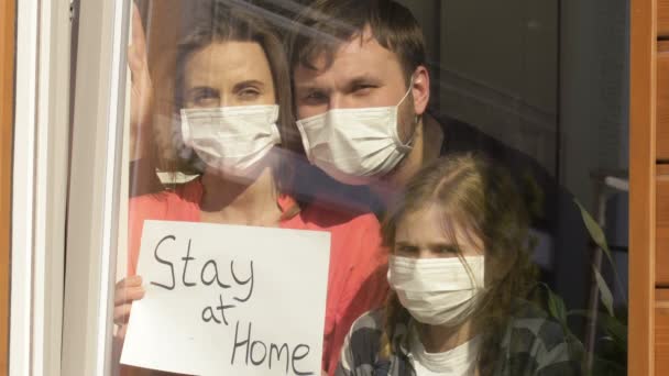 Dreiköpfige Familie steht mit einem Plakat am Fenster. Quarantäne. — Stockvideo