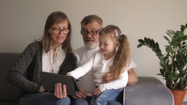 Barn och farföräldrar som använder dator tablett. Älskade medelålders par och deras lilla barnbarn använder en digital surfplatta tillsammans hemma. Pensionärer och modern teknik. — Stockvideo