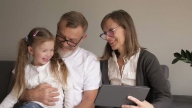 Çocuk ve büyükanne bilgisayar tableti kullanıyor. Sevgili orta yaşlı çift ve küçük torunları evde dijital tablet kullanıyorlar. Yaşlılar ve modern teknoloji..